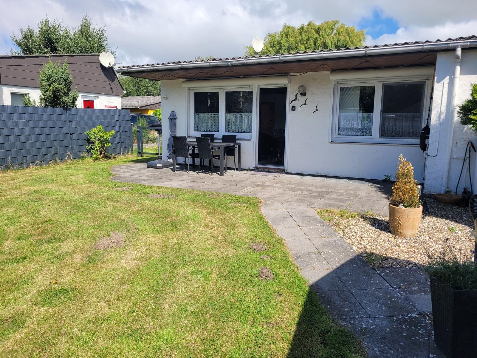 Hinterhof mit Terrasse, Garten und Sitzgelegenheit. Haus mit Fenstern und Tür.
