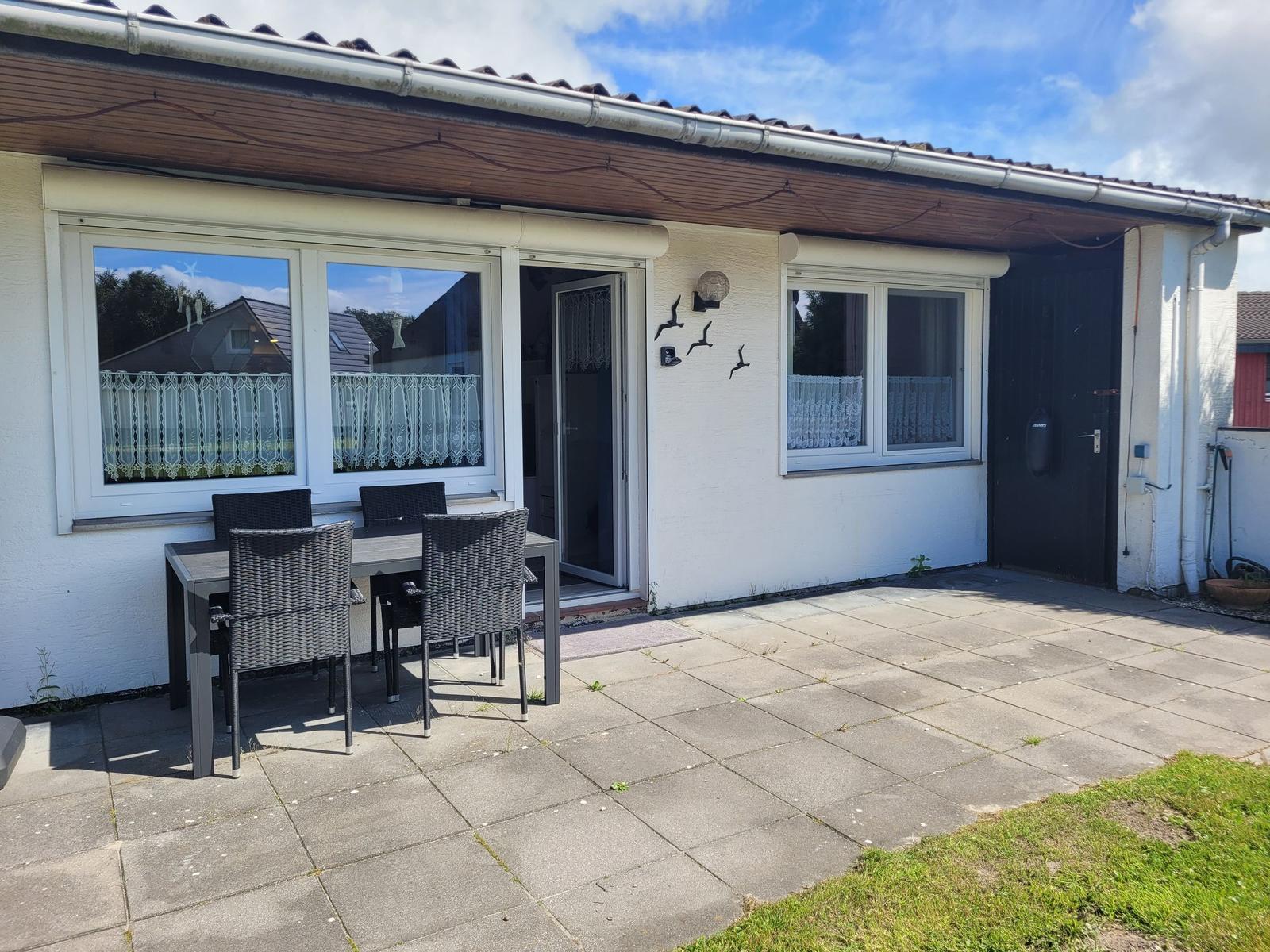 Terrasse mit Tisch und Stühlen vor einem Haus mit Fenstern und Tür.