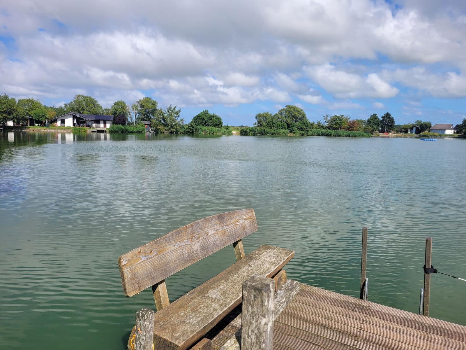 Holzbank am Seeufer mit Blick auf ruhiges Wasser und Uferhäuser.