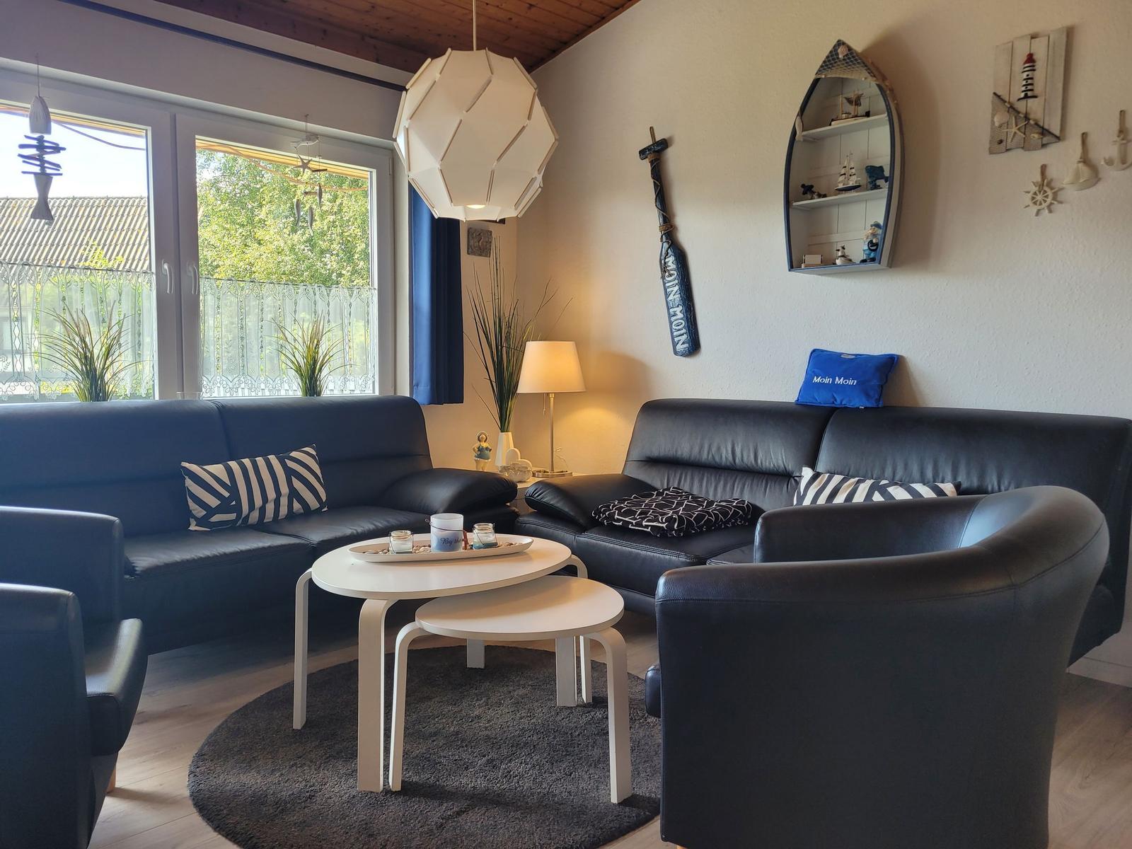 Ein Wohnzimmer mit zwei schwarzen Sofas, einem runden Tisch und Fenstern.