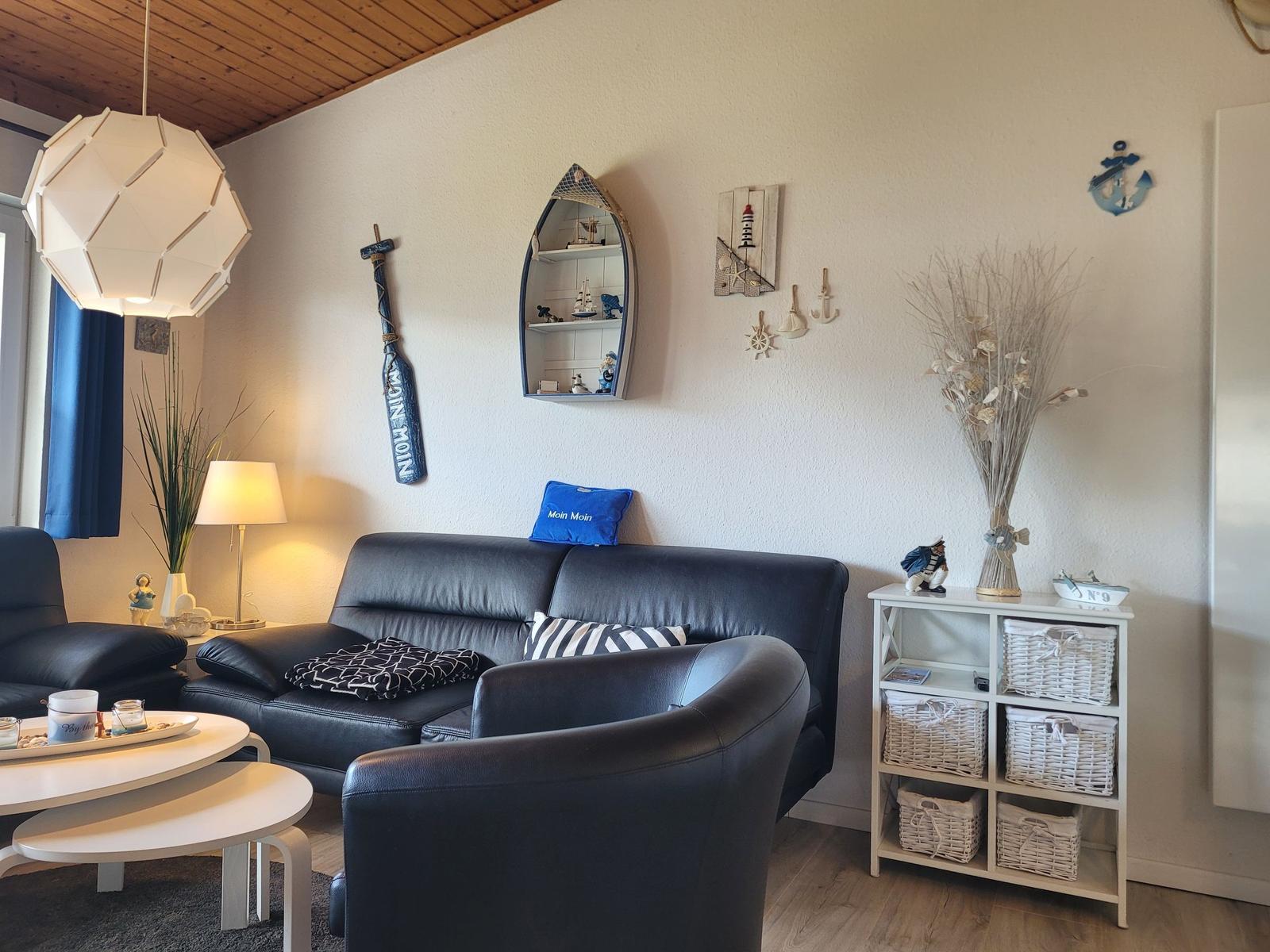 Wohnzimmer mit Sofa, Sessel und dekorativen Meeresmotiven an der Wand.