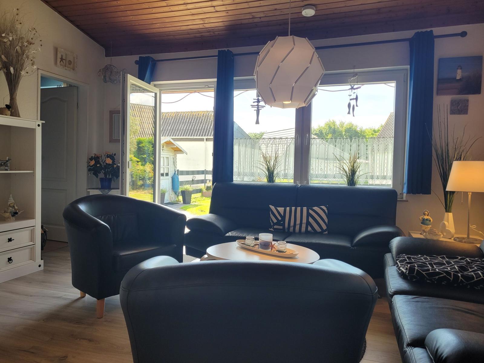 Wohnzimmer mit blauem Sofa, Sitzgelegenheiten und Blick auf den Garten.