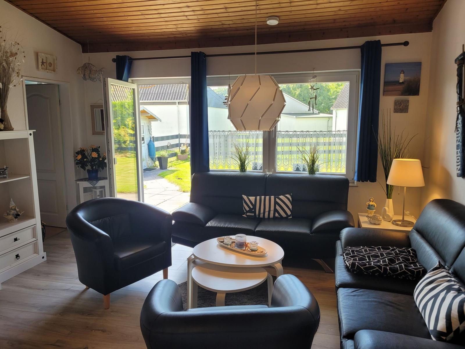 Wohnzimmer mit schwarzen Ledermöbeln, Holzdecke und Blick auf Garten.