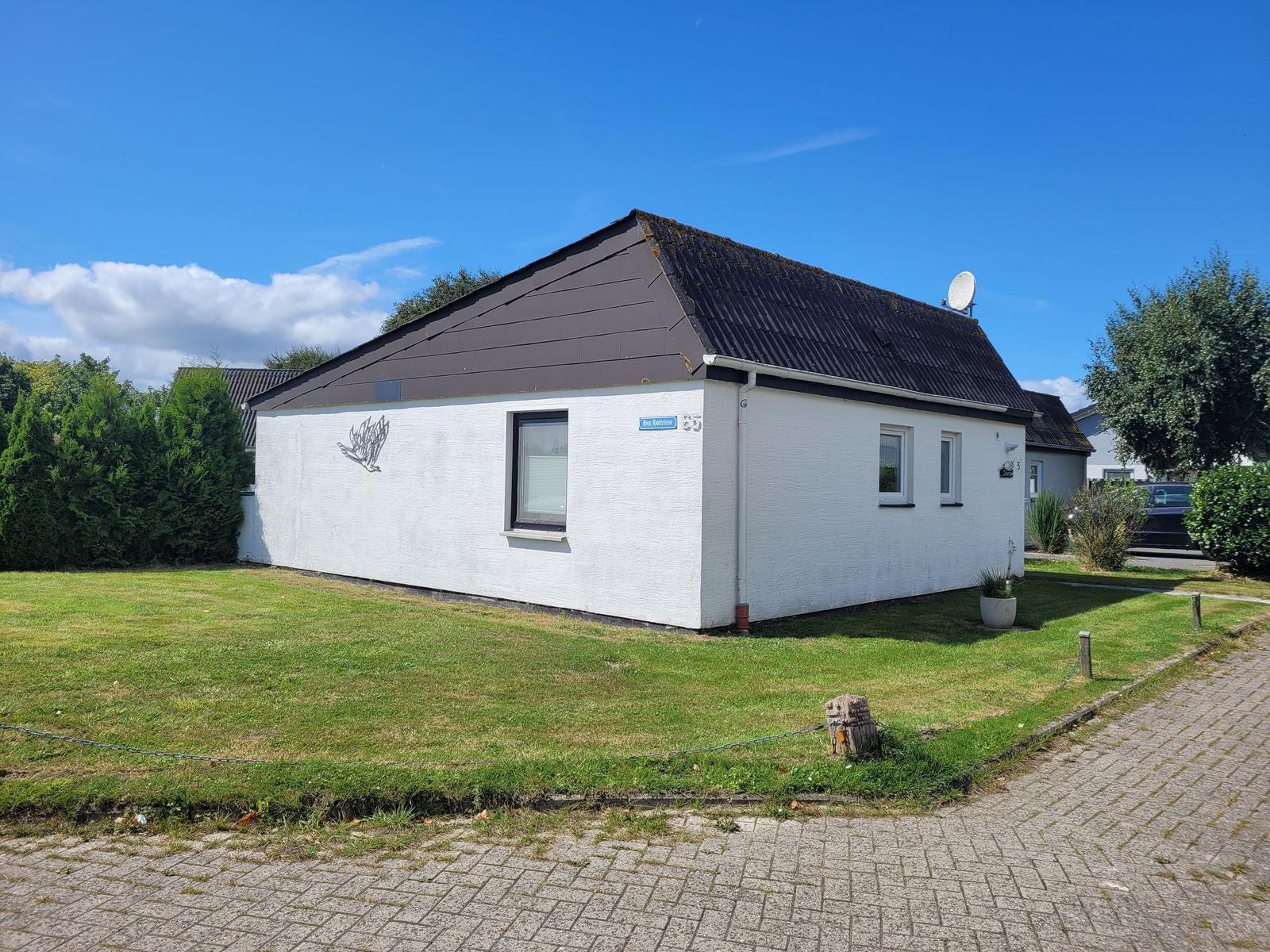 Weiße Ferienwohnung mit Dach und Garten. Satellitenschüssel auf dem Dach.
