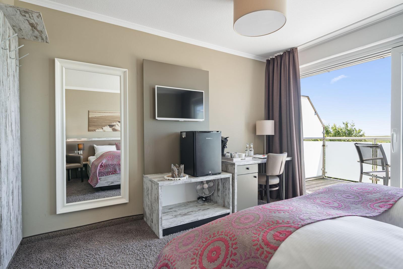 Zimmer mit Bett, Fernseher, Kühlschrank und Balkon mit Blick.