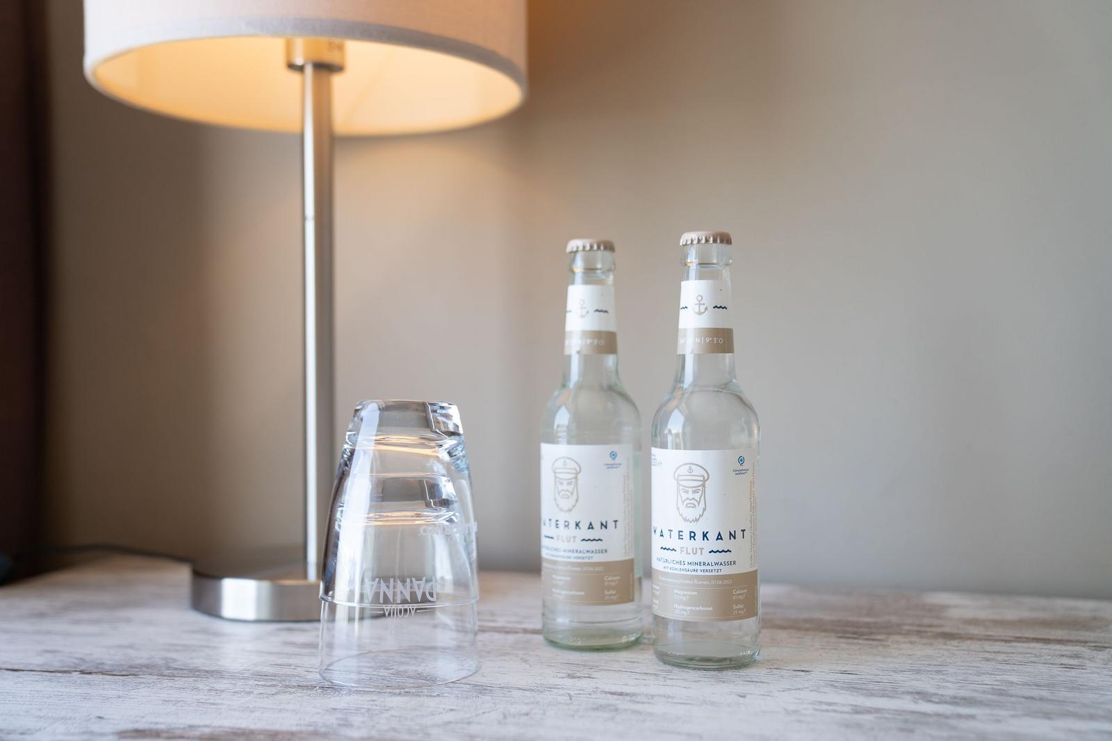 Auf dem Tisch stehen zwei Wasserflaschen und ein Glas neben einer Lampe.