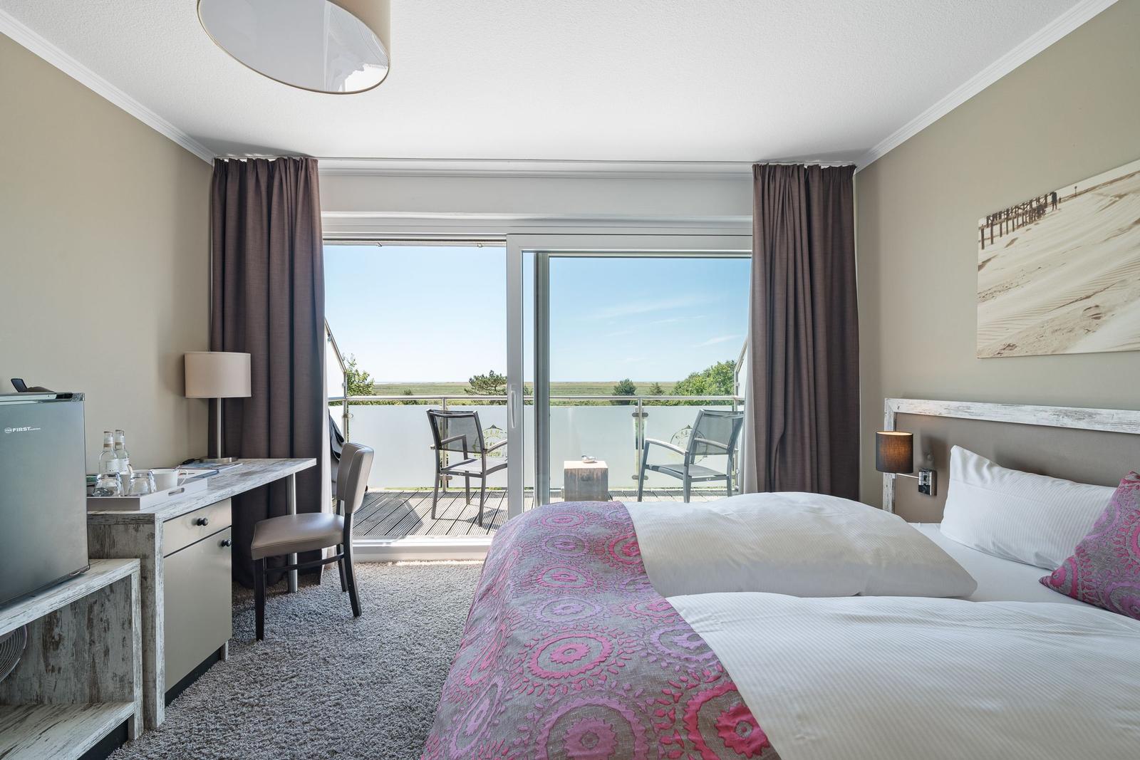 Schlafzimmer mit Balkon, Bett, Schreibtisch und Kühlschrank.