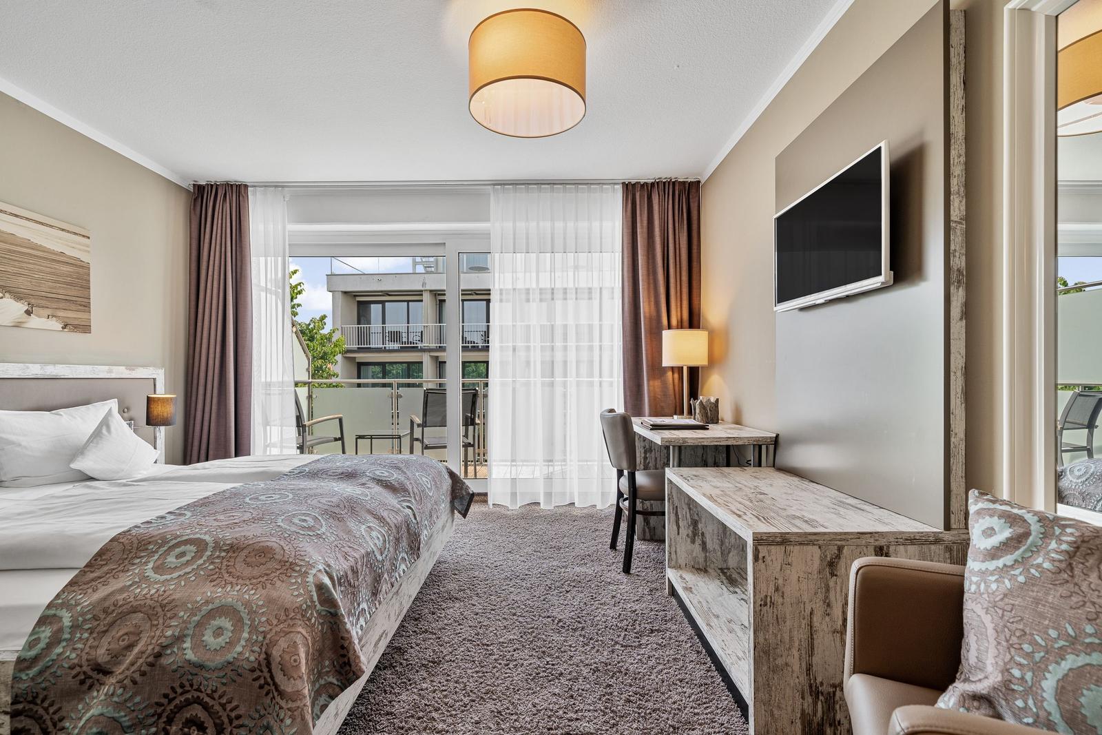 Schlafzimmer mit Bett, Schreibtisch und TV. Balkon mit Sicht auf Gebäude.