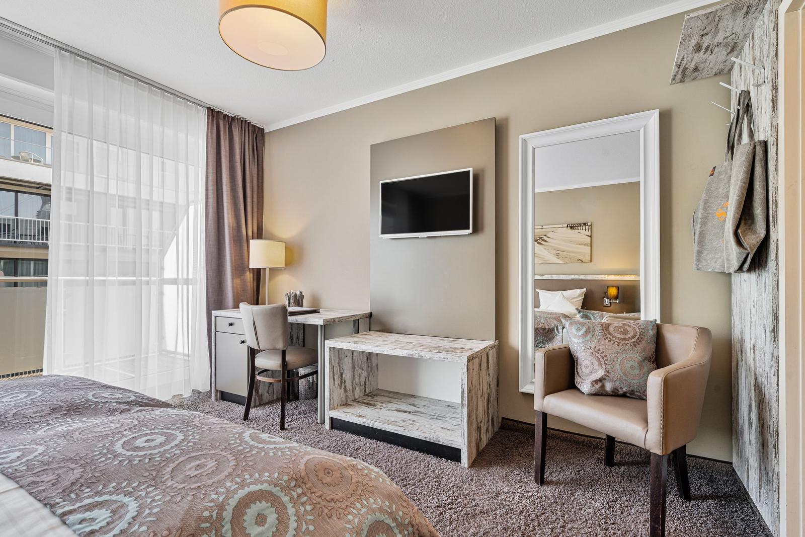 Schlafzimmer mit Bett, Schreibtisch, Fernseher und Sessel.