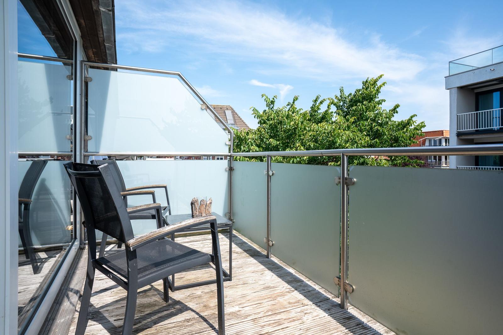 Terrasse mit Stühlen und Tisch, Glasgeländer und Blick auf Bäume.
