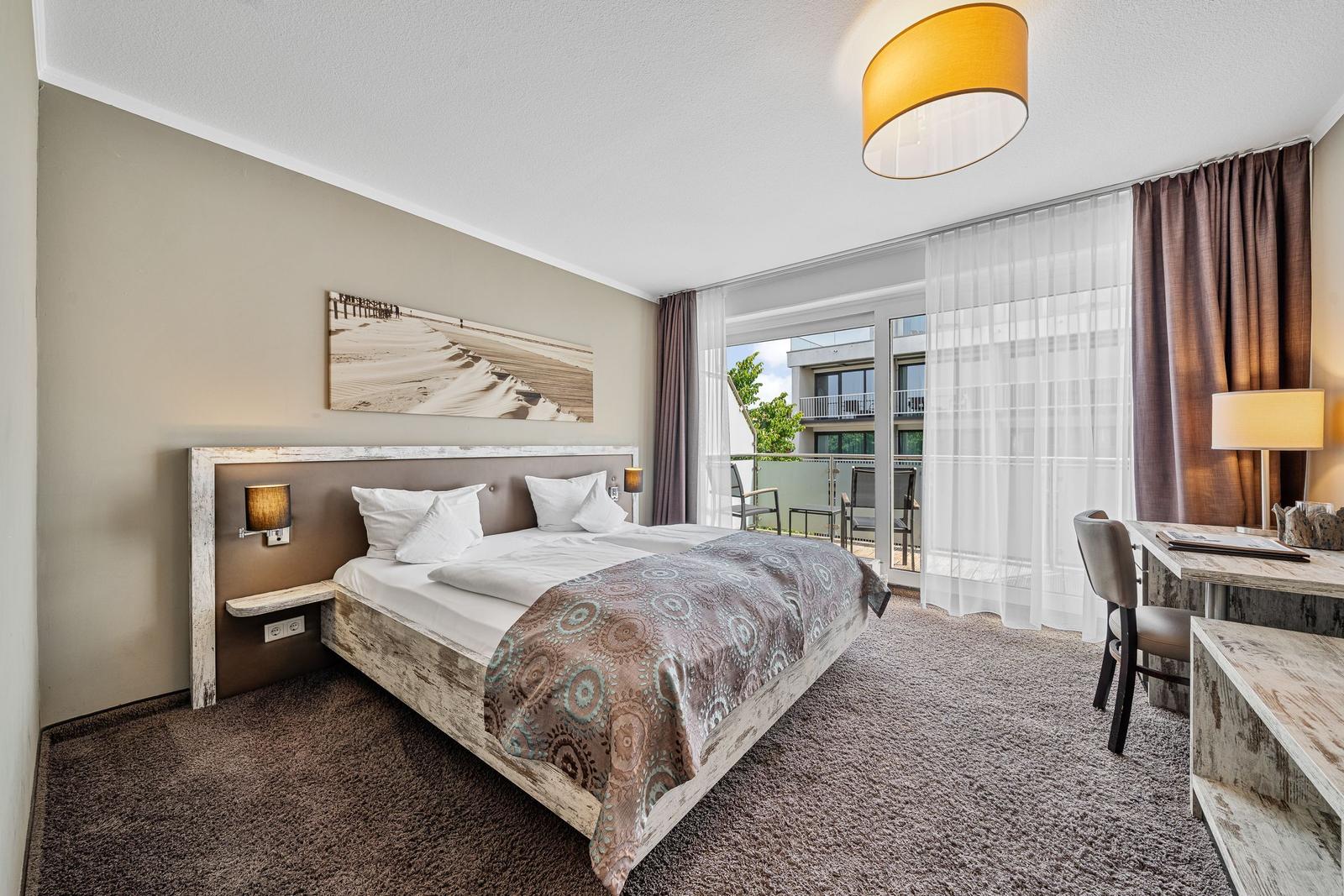 Schlafzimmer mit Doppelbett, Schreibtisch und Balkonansicht.