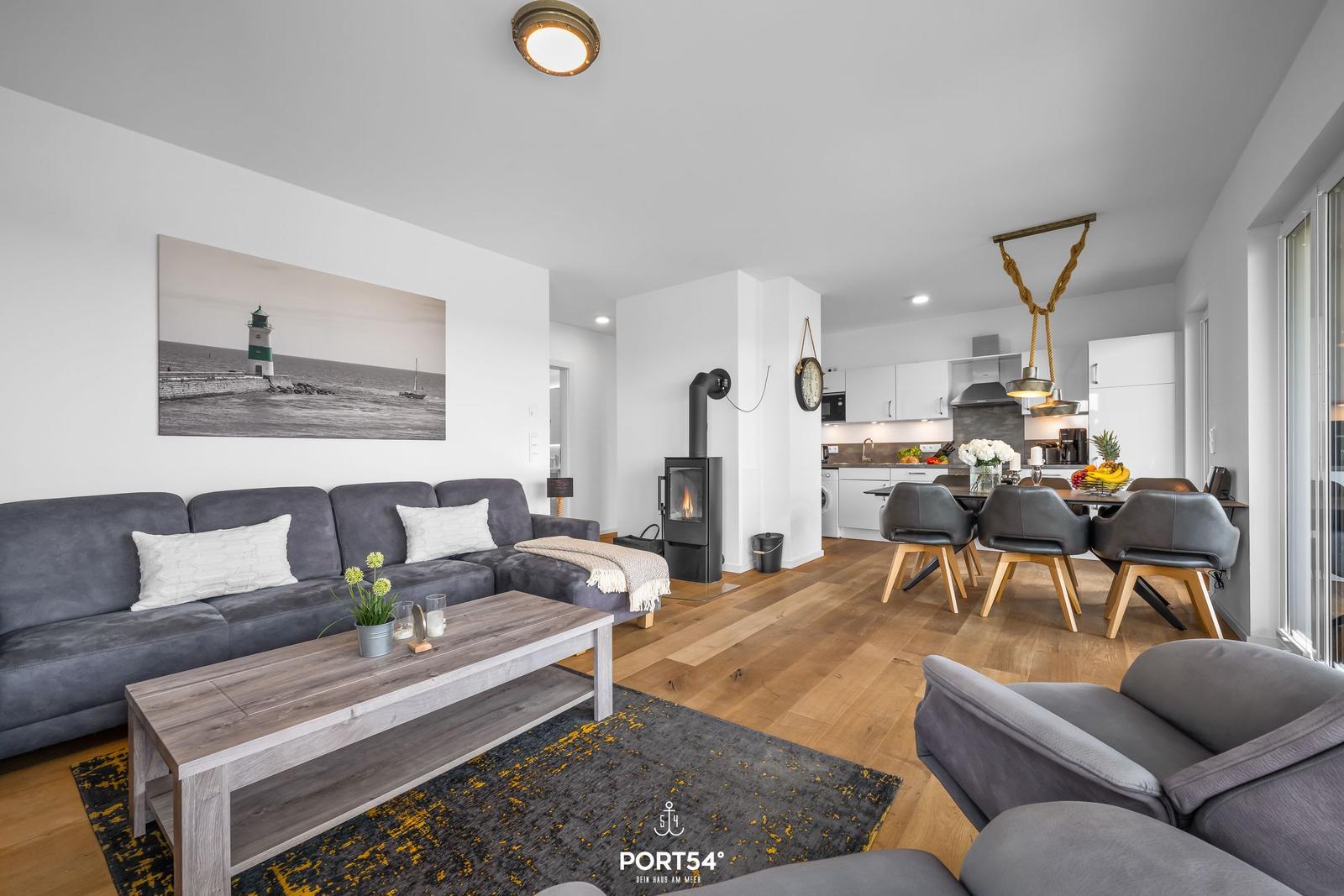 Wohnzimmer mit Sofa, Kamin und Essbereich. Holzboden und Küchenzeile sichtbar.