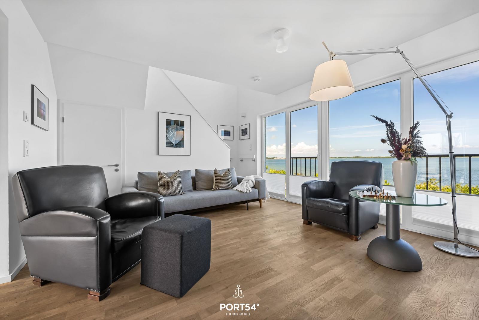 Wohnzimmer mit Blick auf Wasser, zwei Sessel und Sofa.