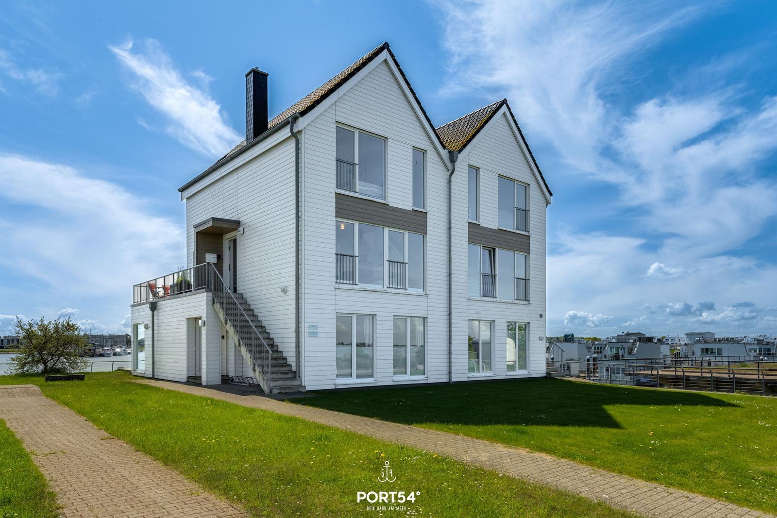 Modernes weißes Haus mit Balkon und Terrasse an Wasser.