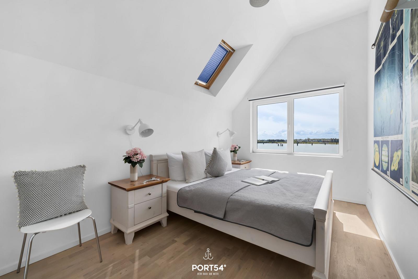 Schlafzimmer mit Bett, Nachttisch und Blick auf Wasser.