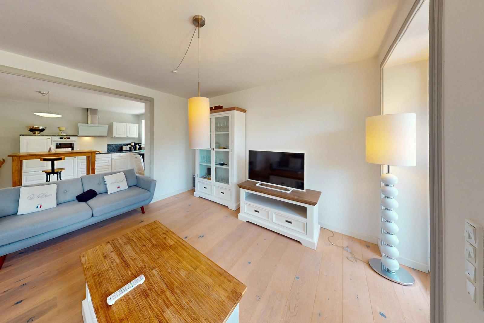 Wohnzimmer mit Sofa, Fernseher und Küchenbereich im Hintergrund.