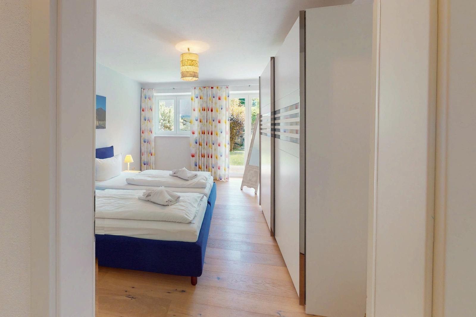 Zimmer mit zwei Betten, Holzboden und Fenster mit bunten Vorhängen.