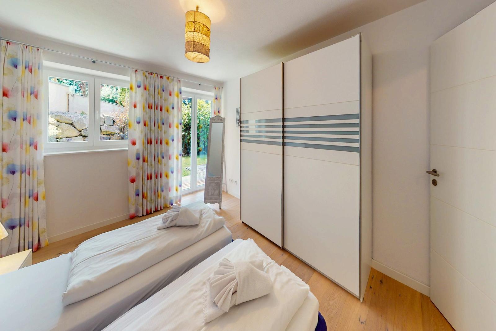 Zwei Betten, Schwebetüren-Schrank und Fenster mit bunten Vorhängen.