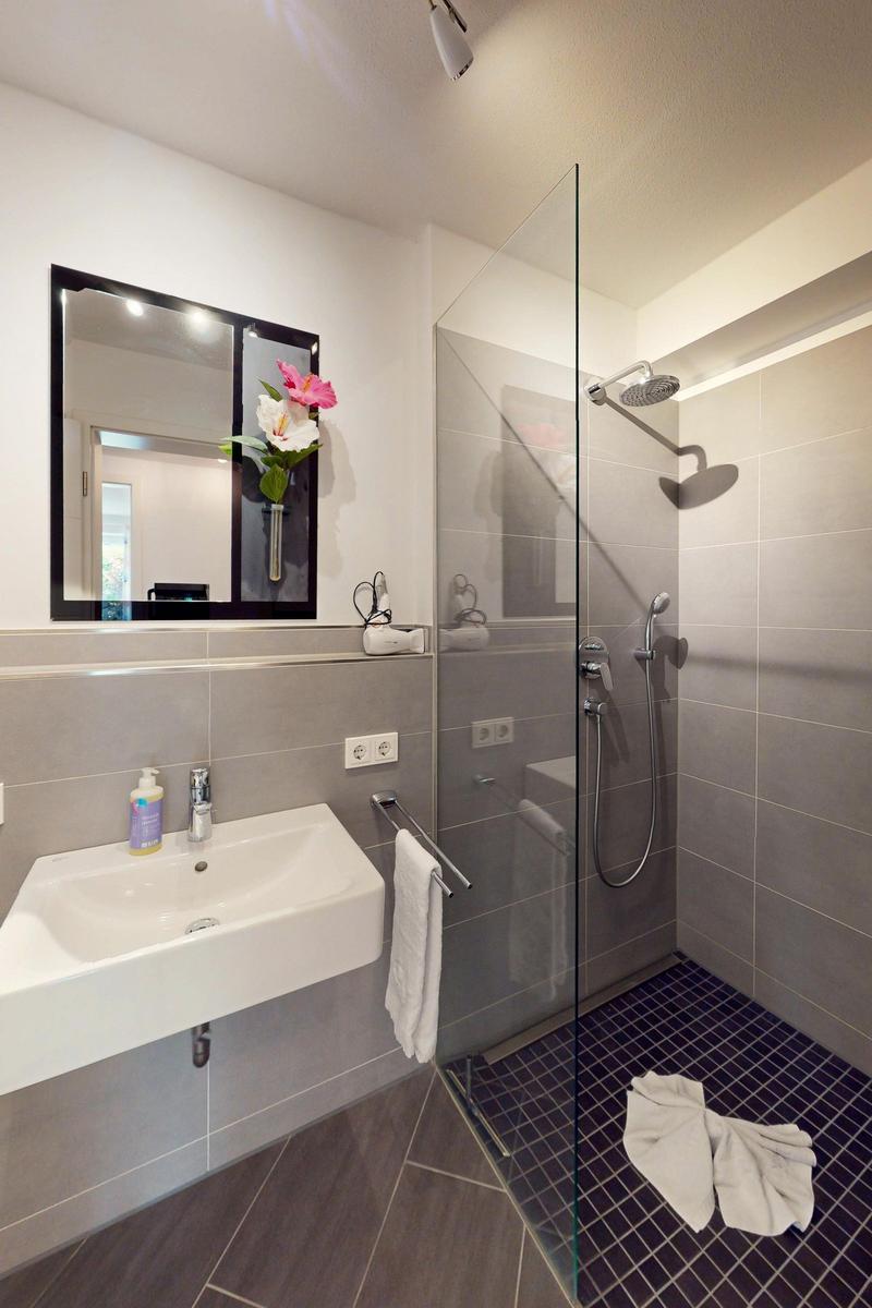 Badezimmer mit Dusche, Waschbecken und Spiegel.