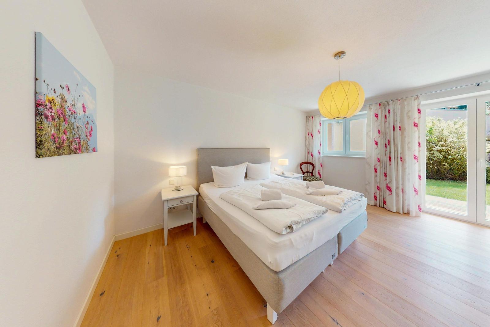 Ein Schlafzimmer mit Doppelbett, Holzboden und Blick auf den Garten.