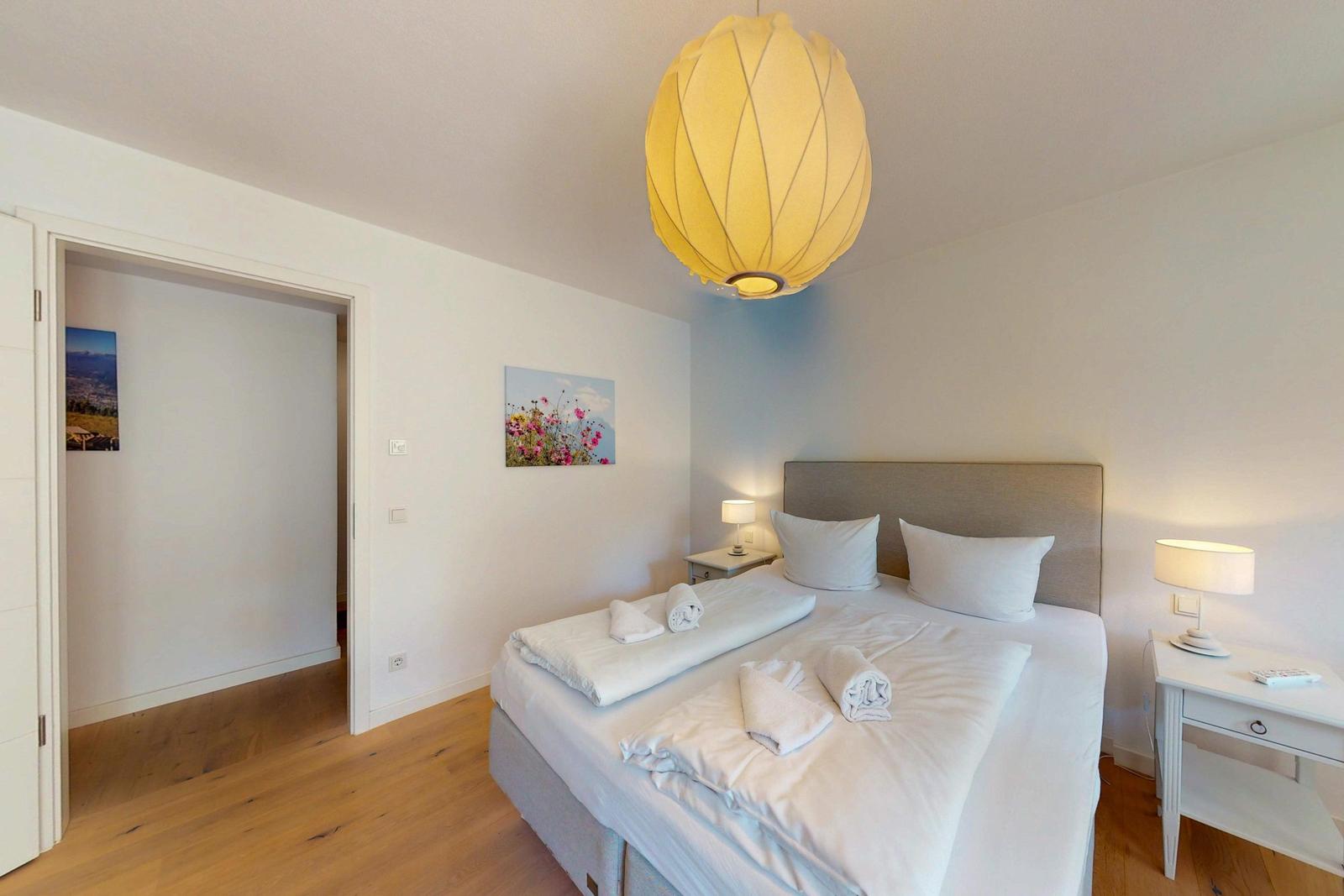 Schlafzimmer mit Bett, Nachttischen und Decke. Hängelampe und Wandbild.