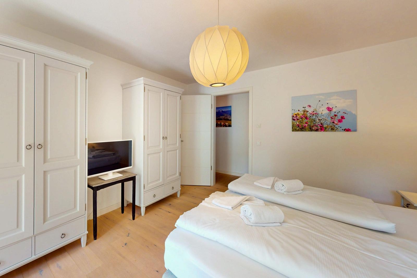 Zimmer mit zwei Betten, weißen Schränken und Holzboden. Hängelampe und Wandbild.