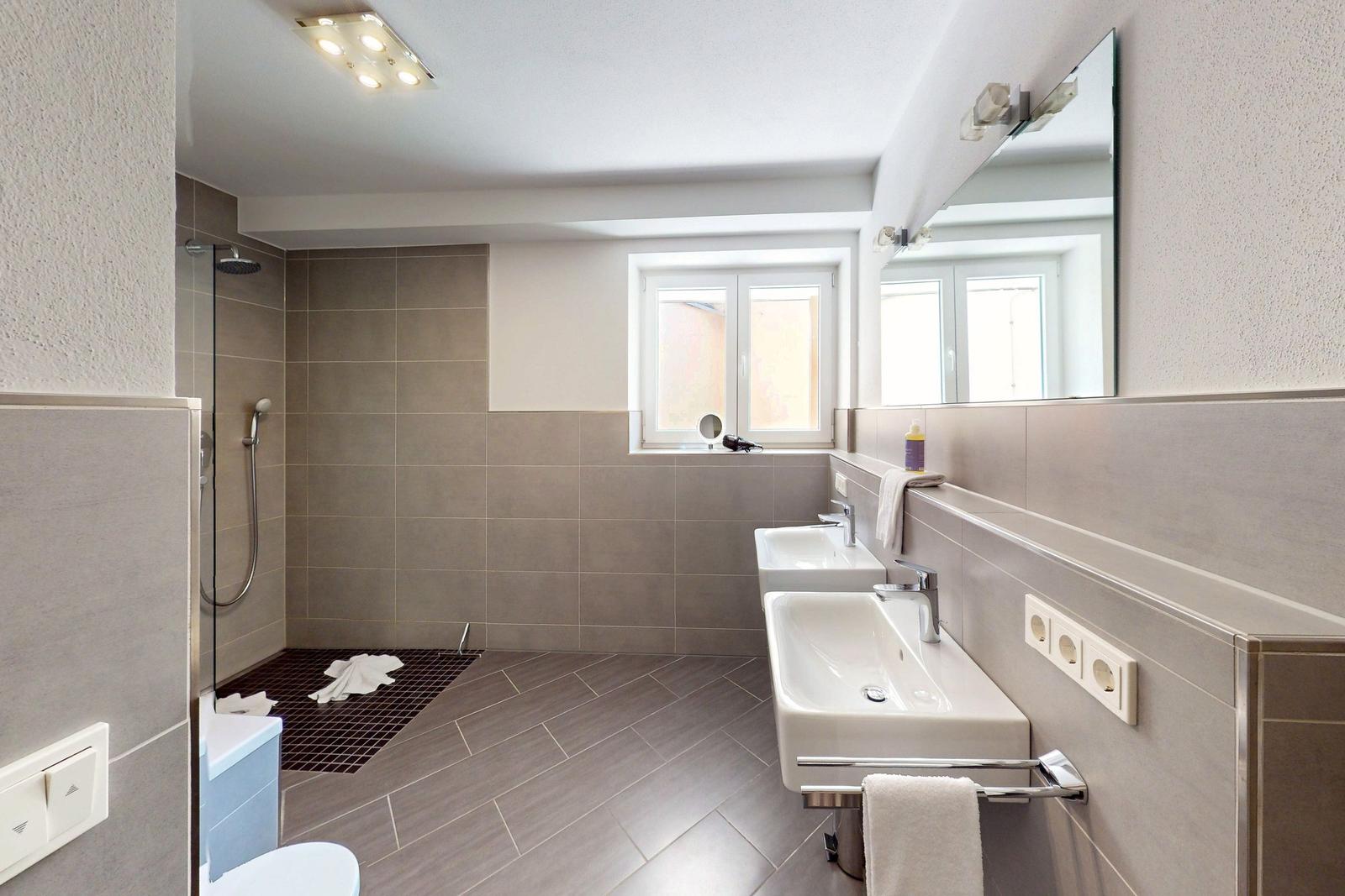 Badezimmer mit Dusche, zwei Waschbecken und Fenster
