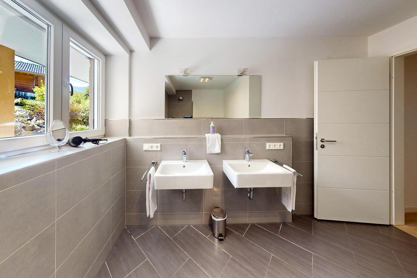 Badezimmer mit zwei Waschbecken, Spiegel und Fensterblick auf Garten