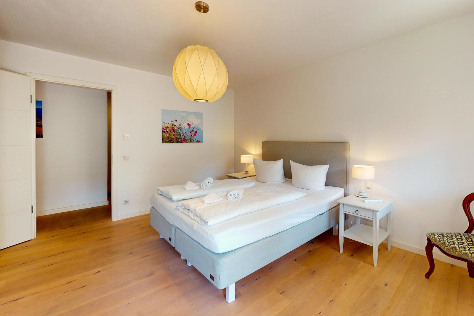 Schlafzimmer mit Bett, Nachttischen und Stuhl auf Holzboden.