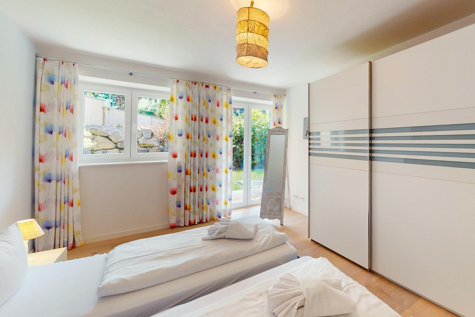 Zwei Betten, Gardinen, Schrank und Fenster mit Blick auf Garten.