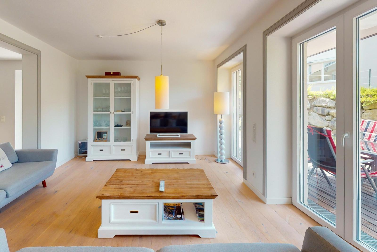 Wohnzimmer mit Holzboden, TV, Couch und Terrasse.