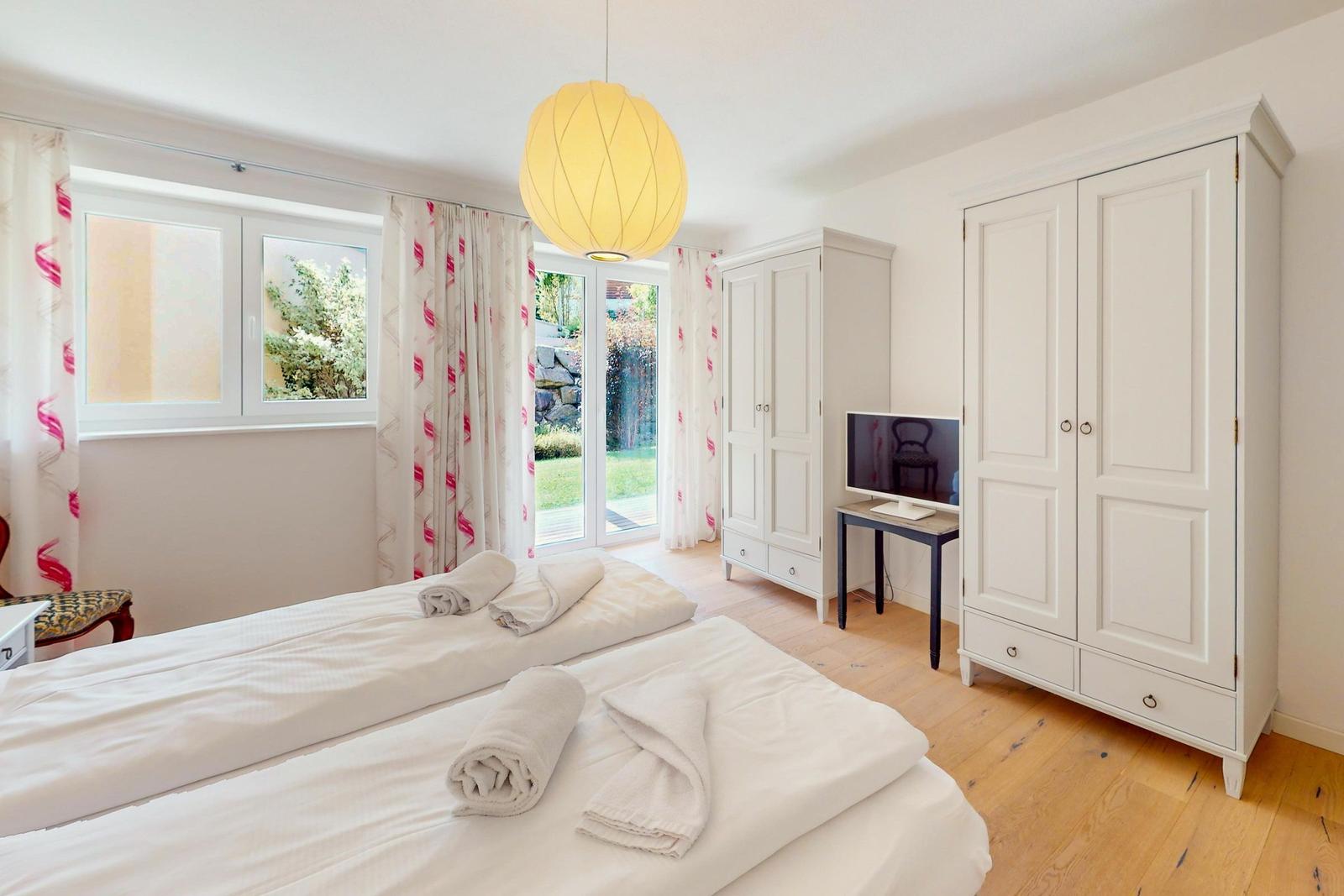 Zwei Betten mit weißen Laken, weiße Schränke, Fenster mit Blick auf Garten.