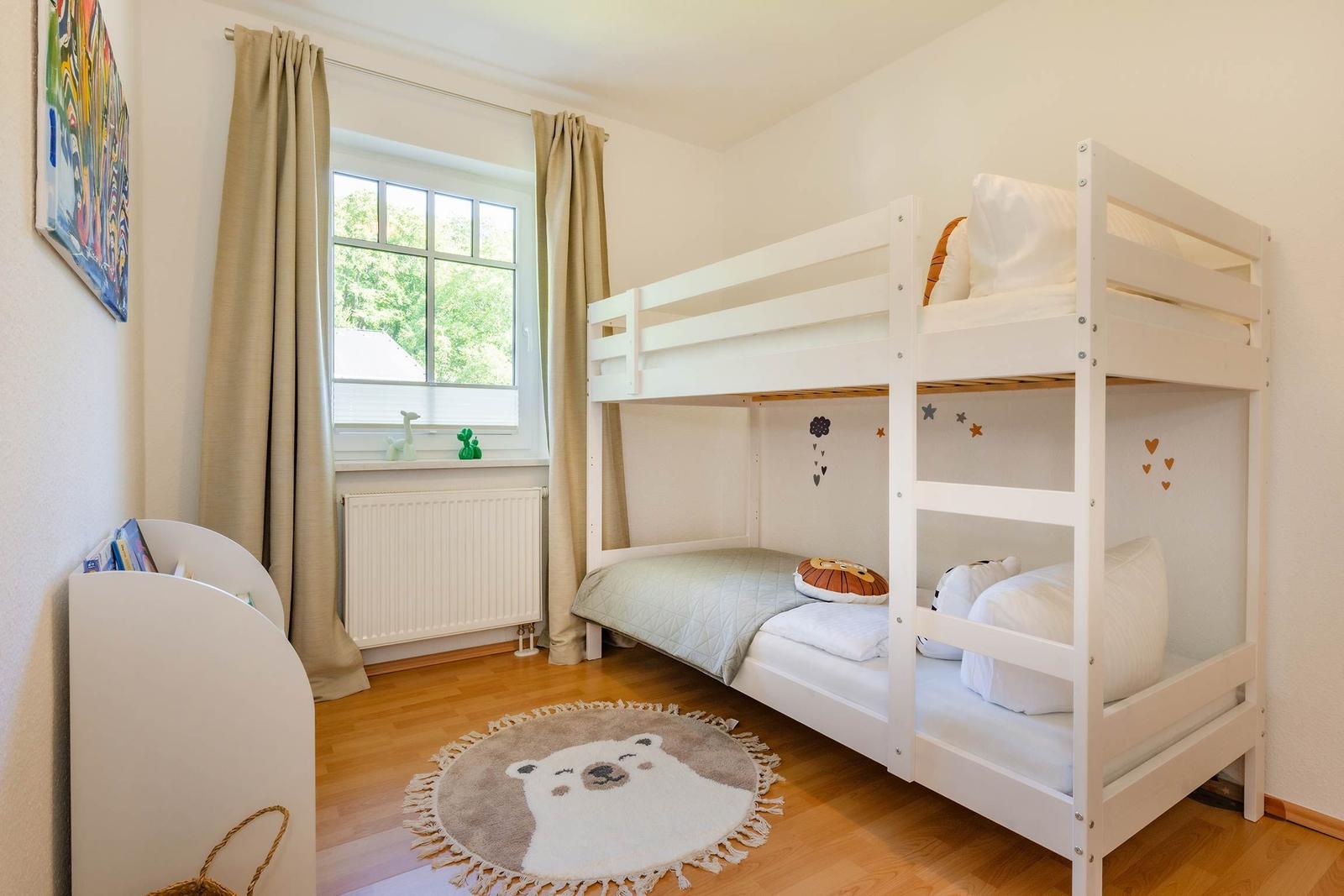 Kinderzimmer mit Doppelstockbett, Fenster, Teppich und Bücherregal.