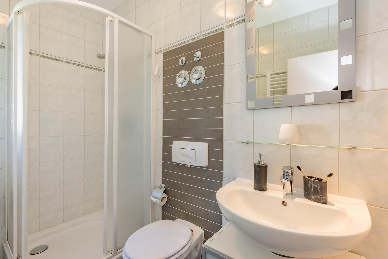 Badezimmer mit Dusche, Waschbecken und Toilette. Fliesen und Spiegel sind sichtbar.