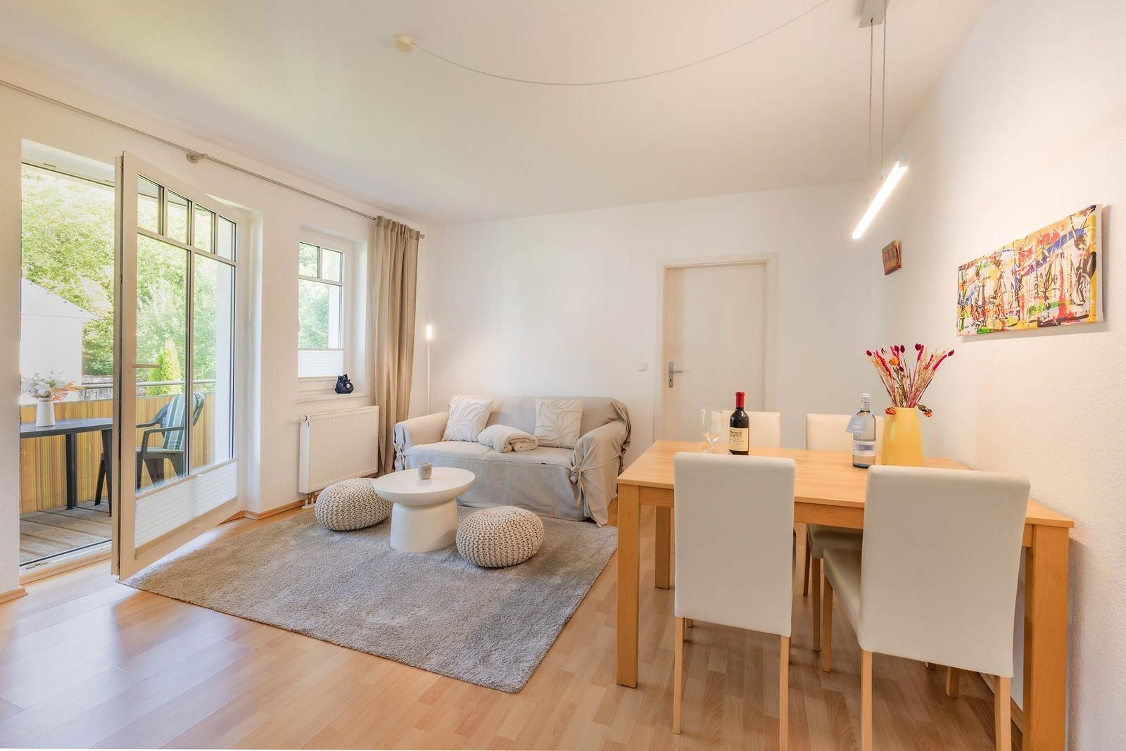 Wohn- und Essbereich mit Sofa, Tisch und Stühlen. Durchgang zur Terrasse mit Blick auf Grün.