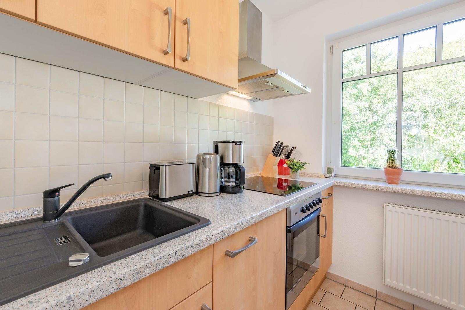 Küche mit Holzschränken, Spüle und Fenster mit Blick auf Grün.