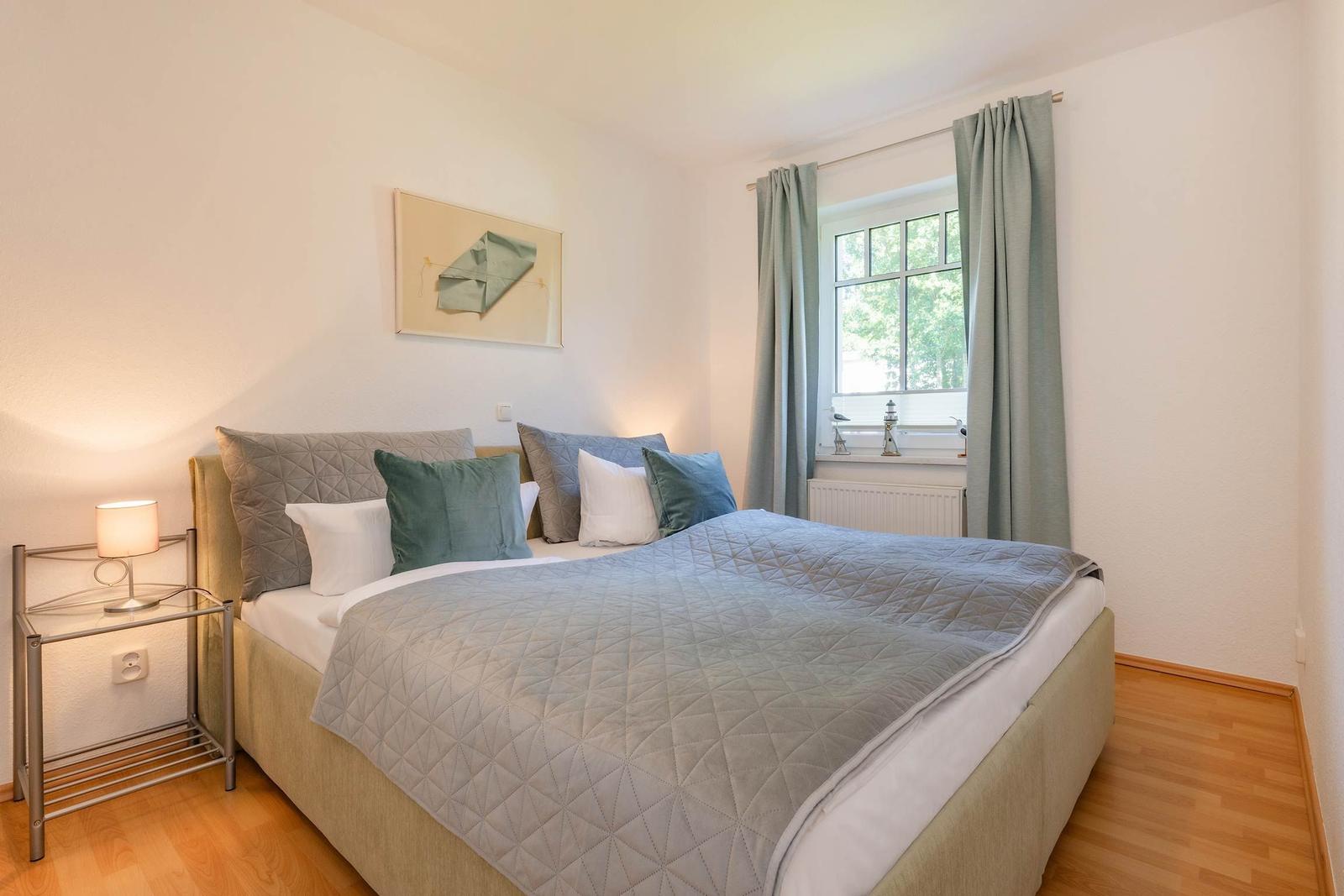 Schlafzimmer mit Bett, Nachttisch und Fenster mit Vorhängen.