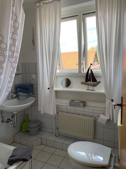 Badezimmer mit Waschbecken, Toilette und Fenster mit Vorhängen.