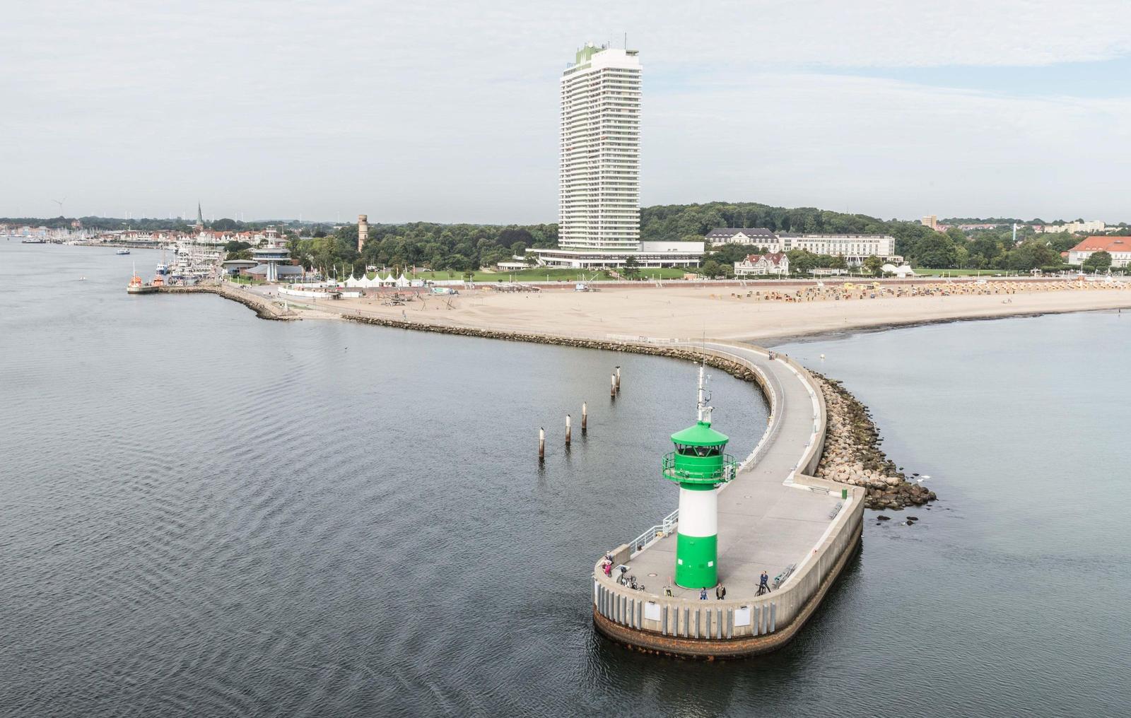Hafen mit Leuchtturm, Strand und Hochhaus im Hintergrund.