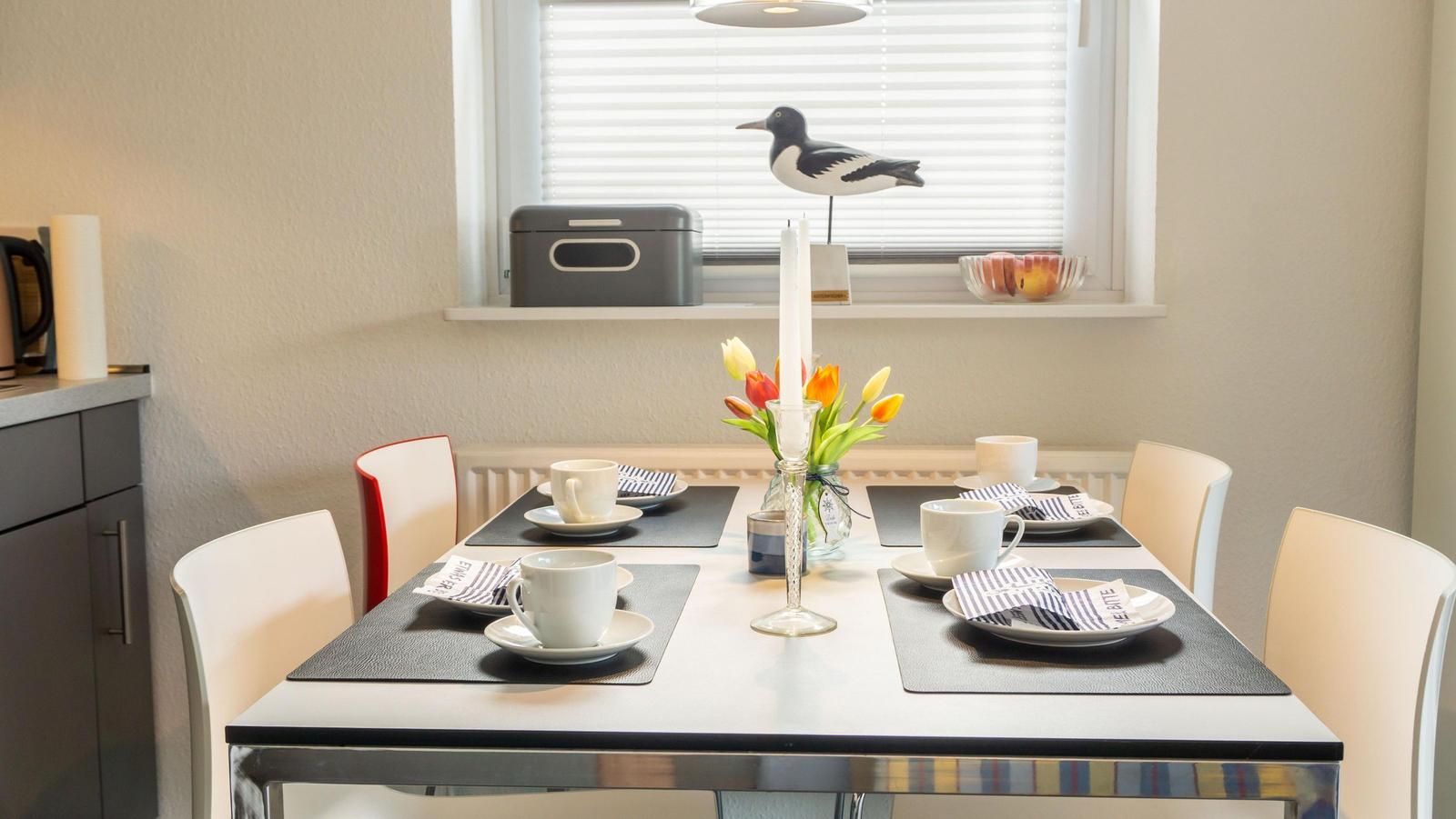 Esstisch mit vier Stühlen, Blumen und Kerzen auf der Fensterbank.