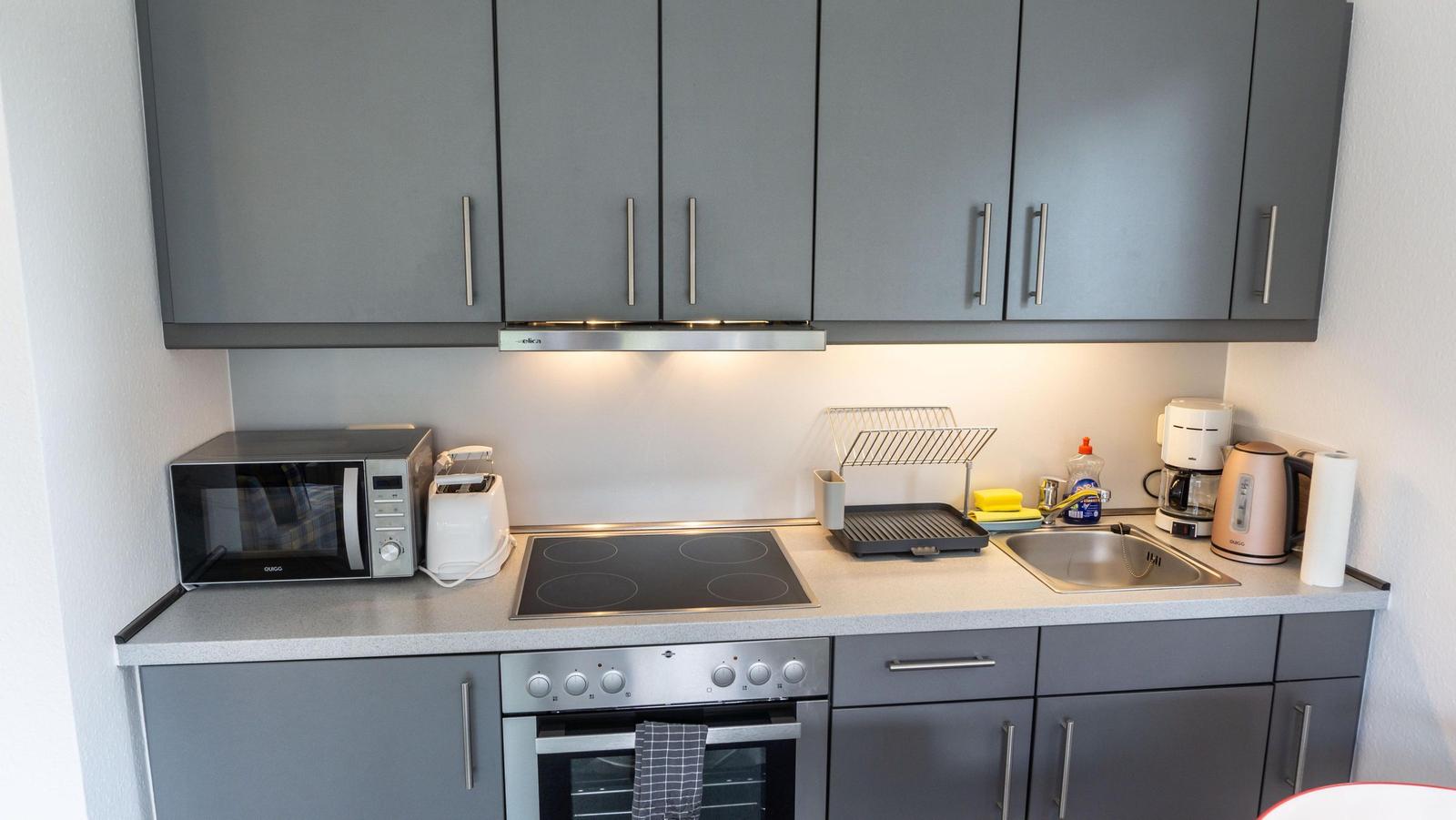 Küche mit grauen Schränken, Herd, Spüle und Küchengeräten.