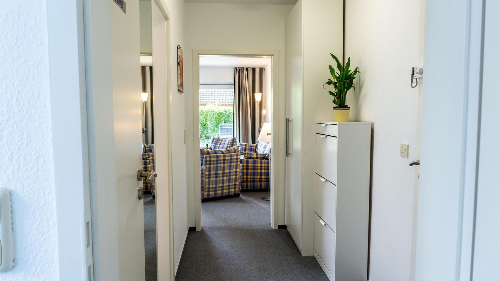 Flur mit weißen Wänden, Pflanze und Blick in Wohnzimmer mit Sofa.