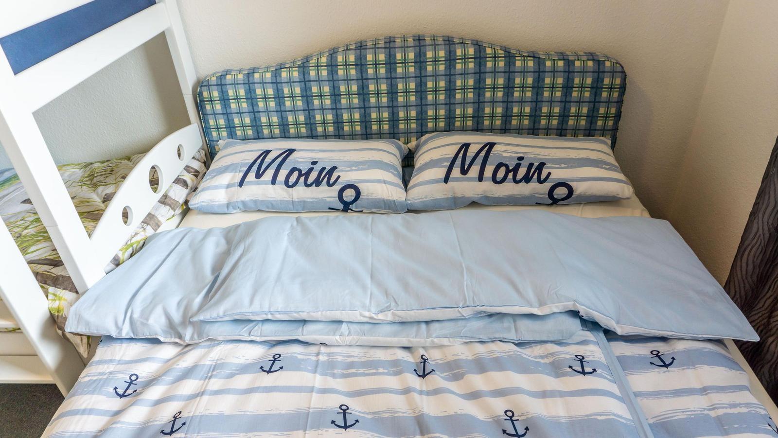 Schlafzimmer mit Bett, Kissen und Decke im nautischen Stil.