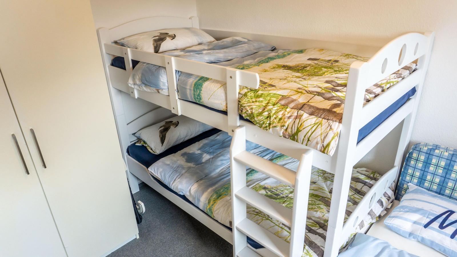 Doppelstockbett mit Matratzen und Bettwäsche. Neben einem Kleiderschrank.