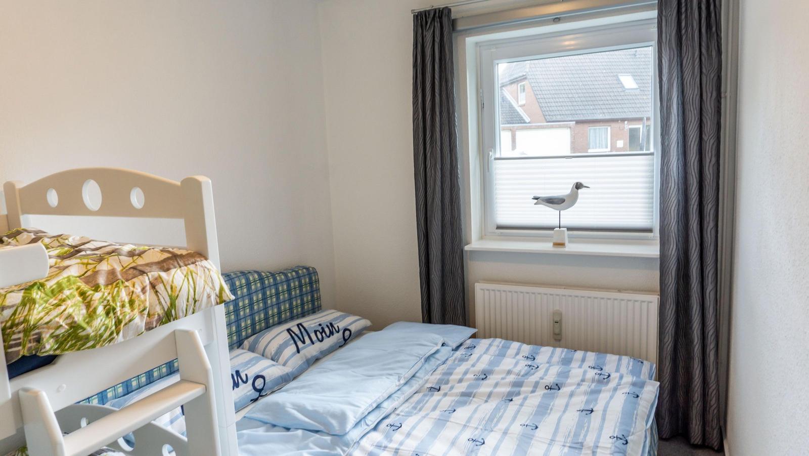 Zimmer mit Doppelbett und Etagenbett, Fenster mit Jalousie und Vogeldekoration.