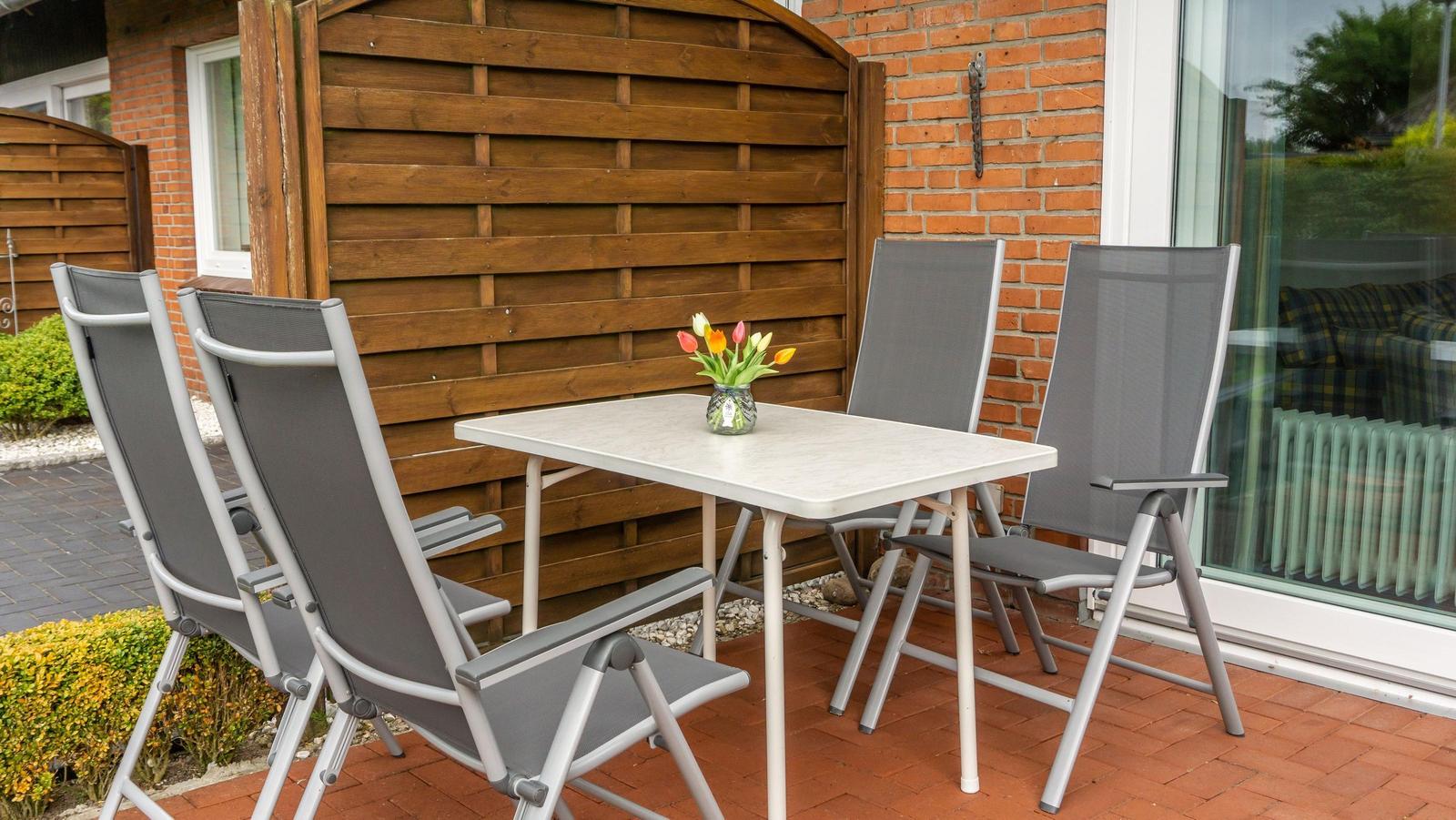 Terrasse mit Tisch und vier Stühlen, Blumen in Vase, Holz- und Ziegelwand