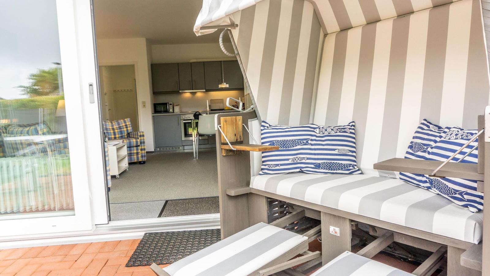 Strandkorb mit Streifenkissen und Blick ins Innere der Ferienwohnung.