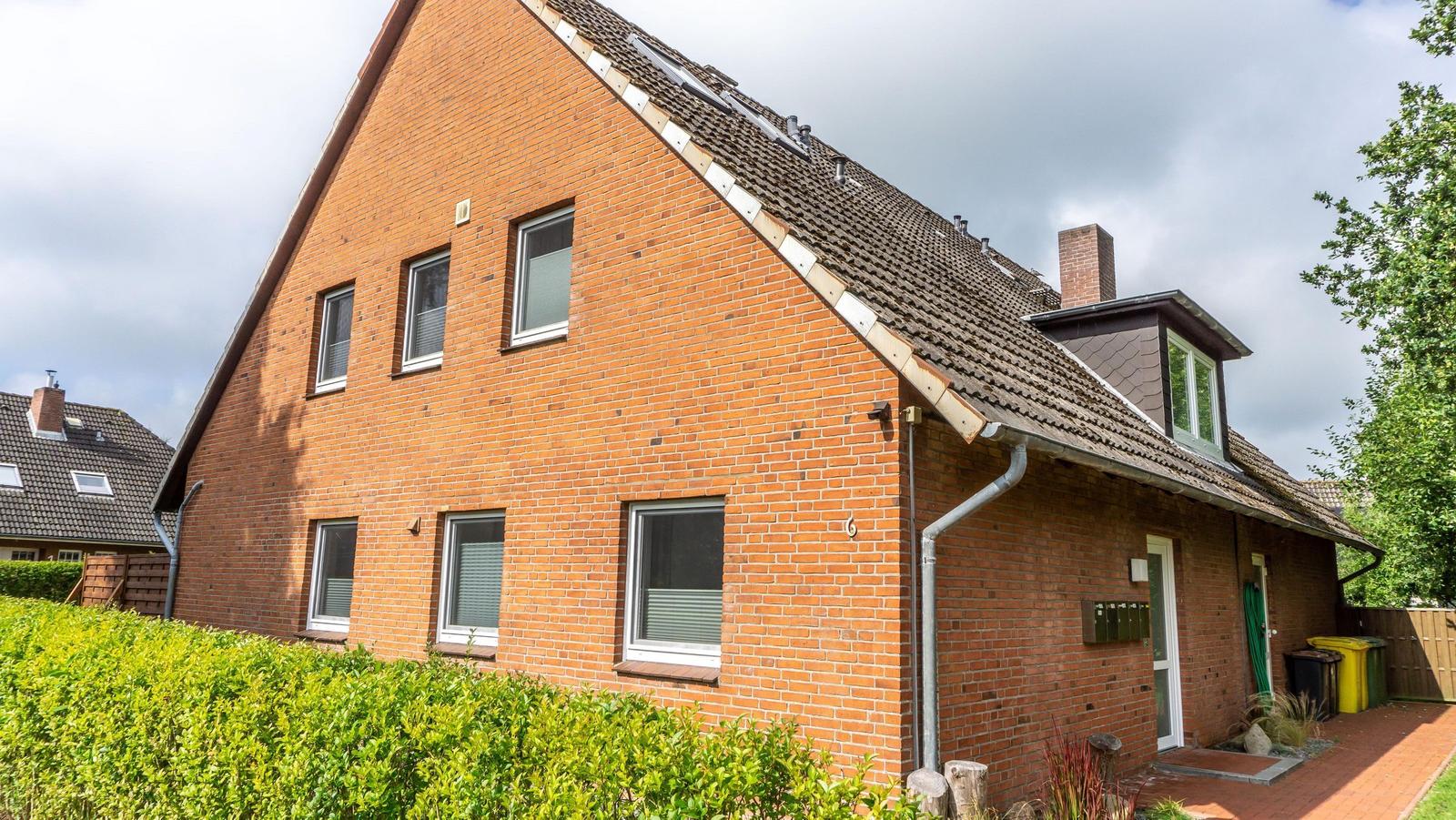 Rotes Backsteinhaus mit Dachgaube und grünem Heckgarten.