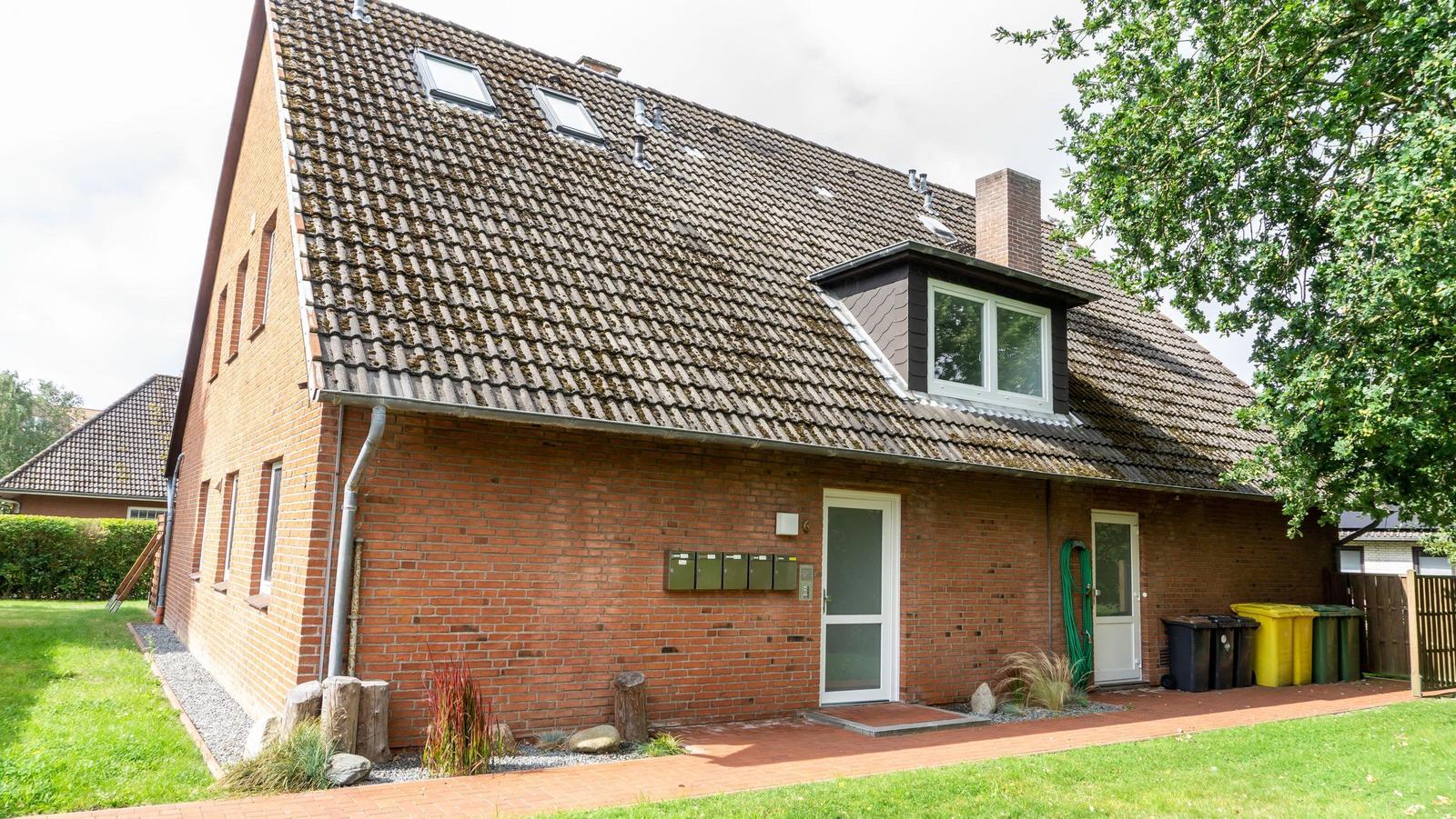 Ein Haus mit Backsteinfassade und Dachgauben. Vorgarten mit Rasen und Pflanzen.