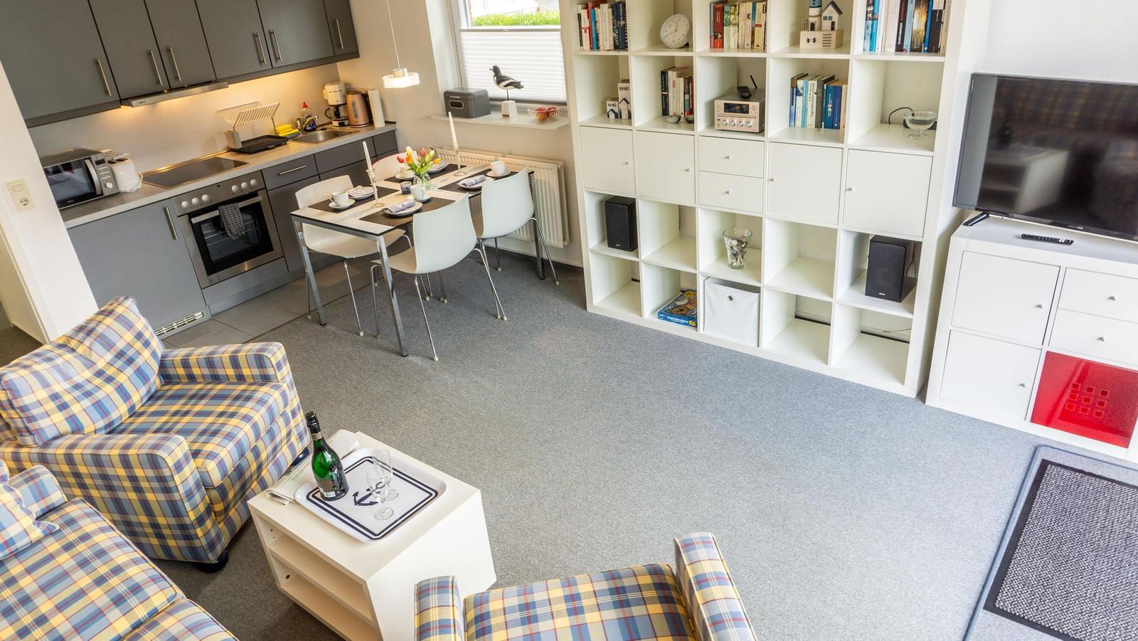 Wohnung mit Küche, Esstisch und Wohnbereich mit Plaid-Sofa und Fernseher.